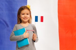 Smiling schoolgirl with flag and textbook against French flag standing against flag of France